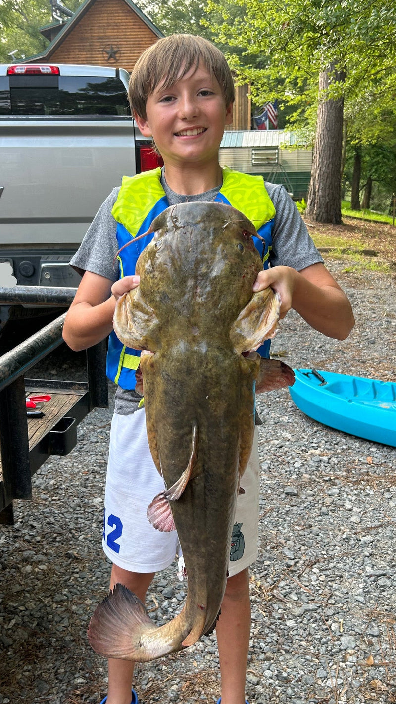 Young boy holding a large fish outdoors near a truck and kayak.